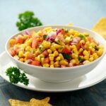 Roasted Corn Salsa in white bowl with lime and tortilla chips.
