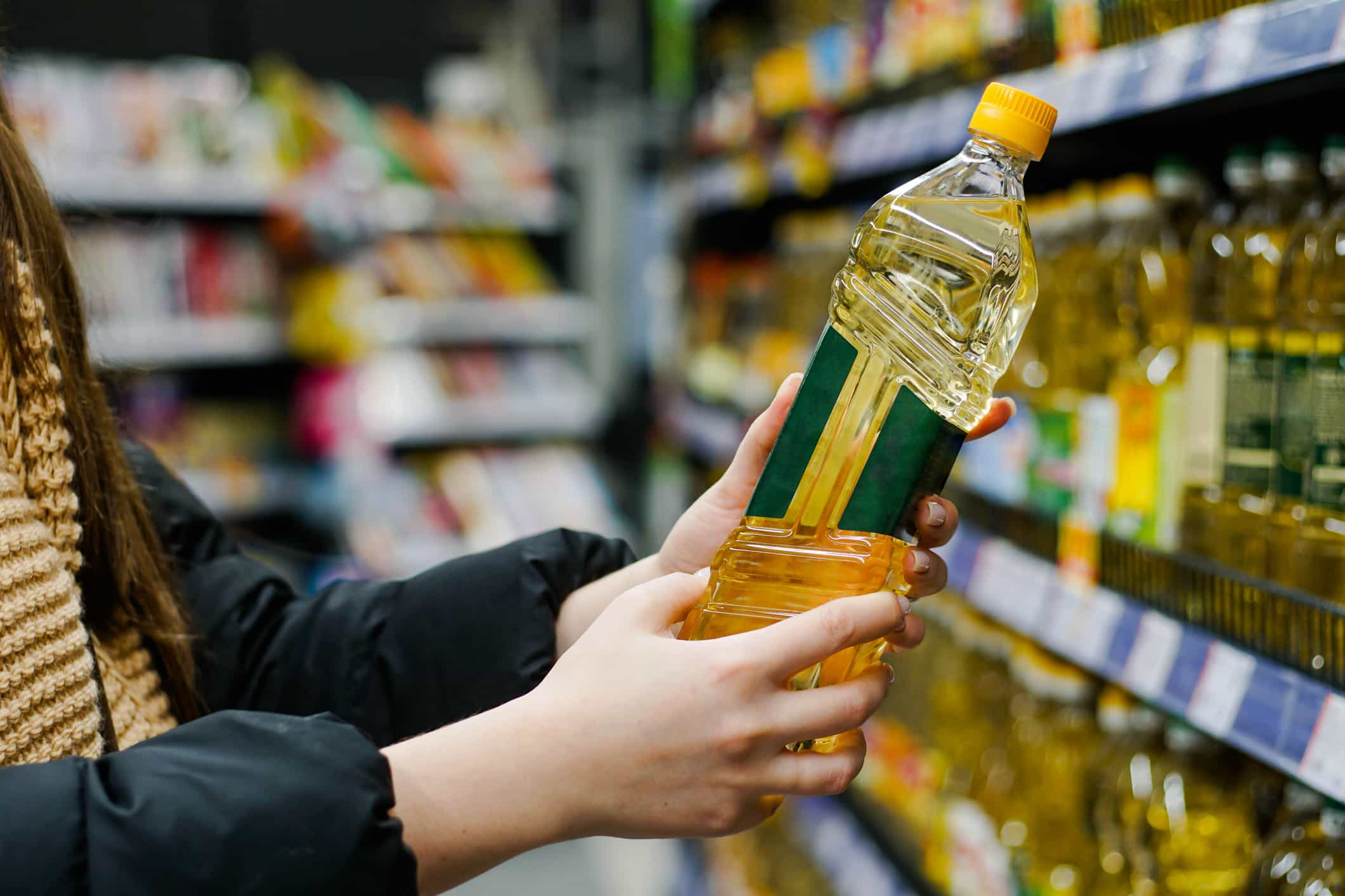 Person Holding Oil in Grocery Store Aisle